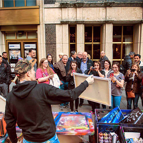 A crowd watching a live outdoor art demonstration